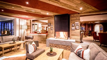 Gemütlicher Wohnraum mit Kamin, Sesseln und Sofas in warmen Holztönen