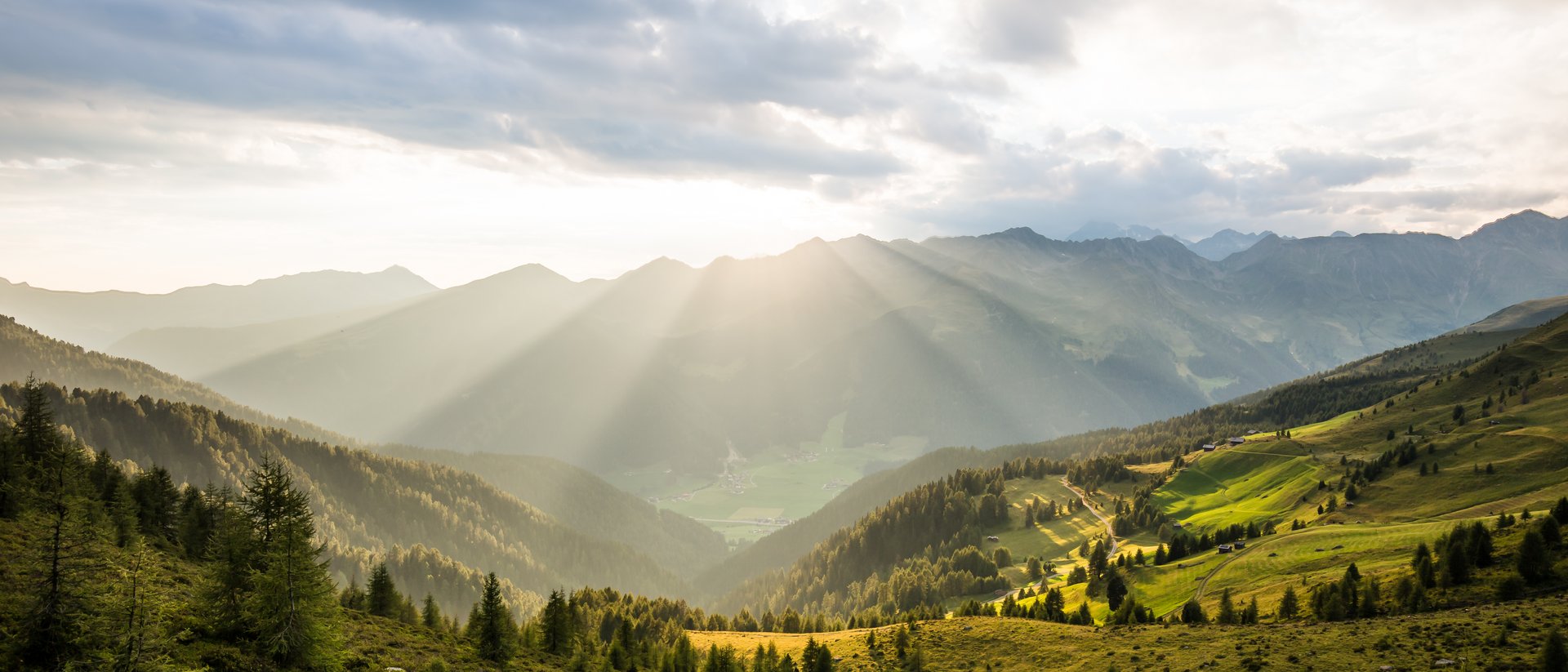 Sonnenstrahlen durch Wolken über grünen Bergen und Tal