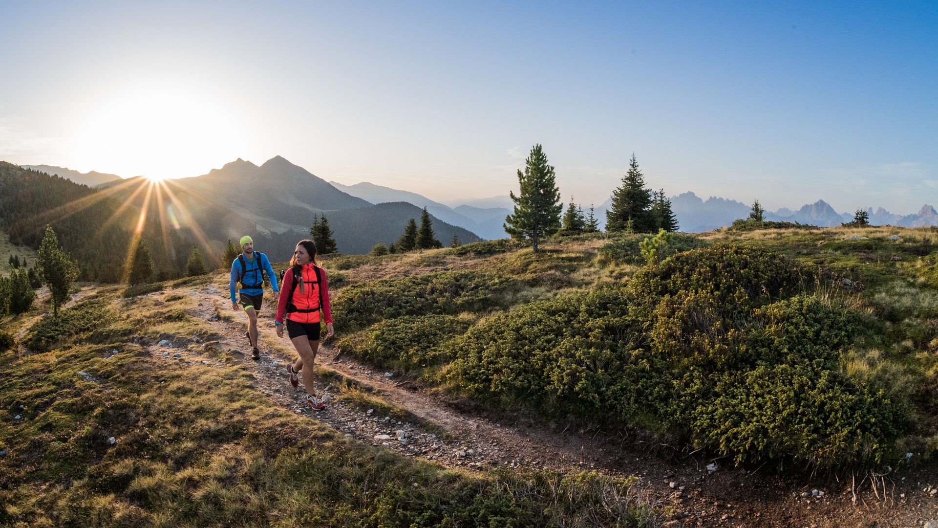 Zwei Wanderer auf Bergpfad bei Sonnenuntergang in einer alpinen Landschaft