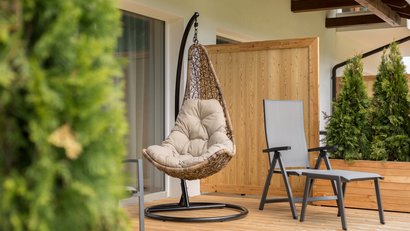 Balcone con poltrona sospesa e sedia sdraio vicino a parete in legno e piante