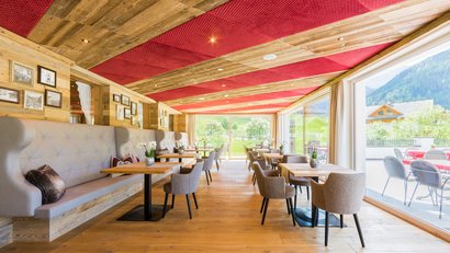 Ristorante luminoso con pavimento in legno, pannelli rossi sul soffitto e grandi finestre con vista montagna