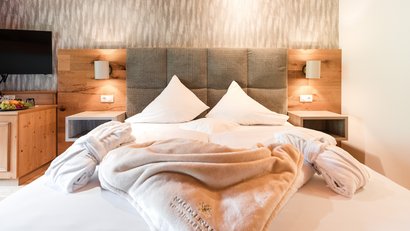 Gemütliches Hotelzimmer mit Bett, Kissen und Bademänteln auf der Decke