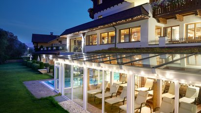 Beleuchtetes Wellnesshotel mit Wintergarten und Liegestühlen am Abend