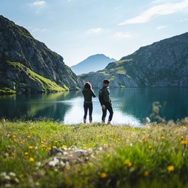 Zwei Menschen stehen an einem See in den Bergen bei klarem Wetter