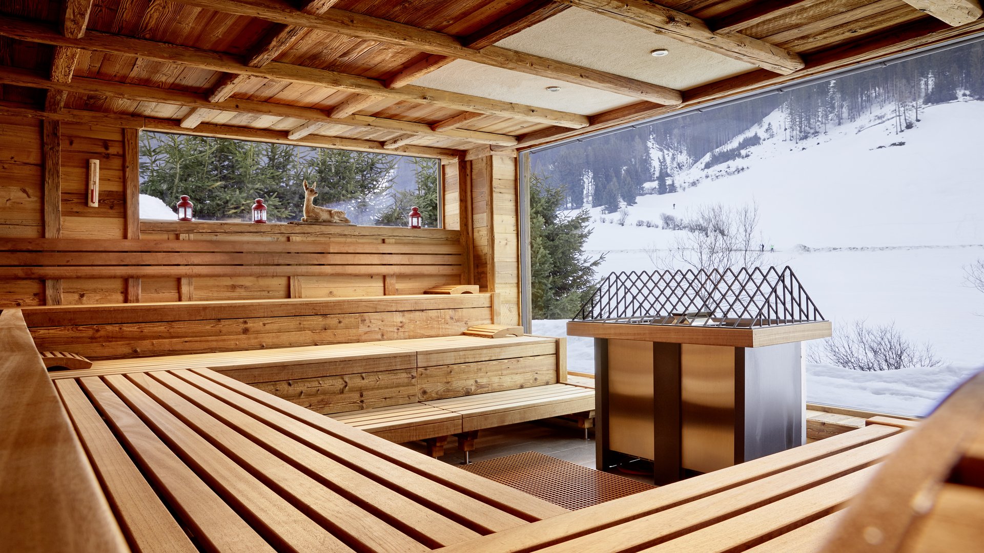 Holzsauna mit großen Fenstern und verschneiter Berglandschaft draußen