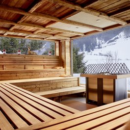 Holzsauna mit großen Fenstern und verschneiter Berglandschaft draußen